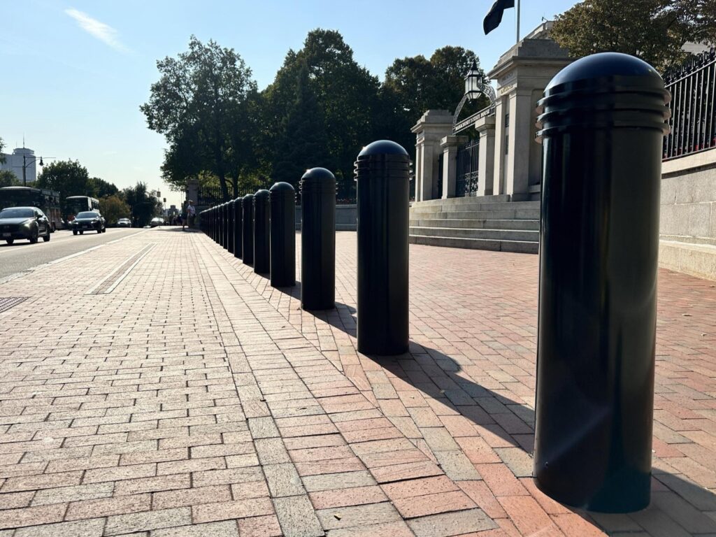 Row of bollards with black decorative covers on the side of a street.