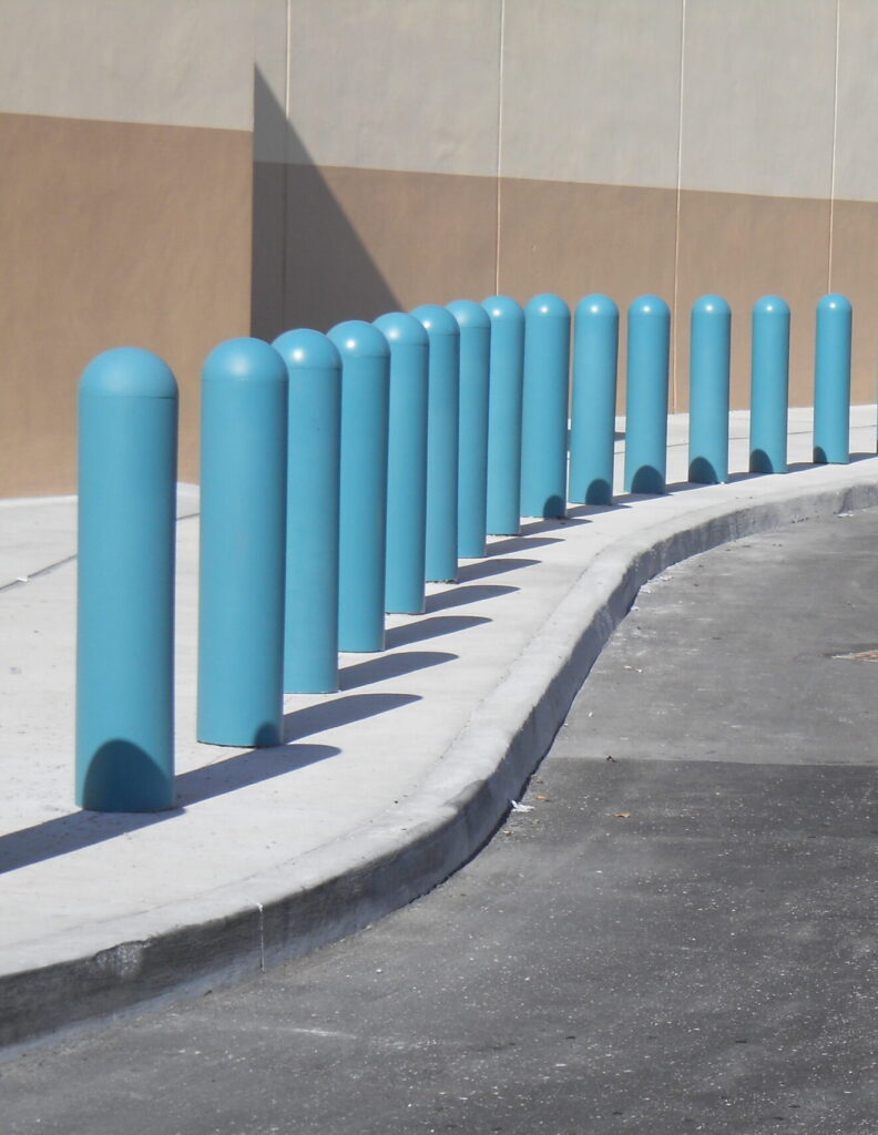 Photo of a row of bollards on a sidewalk. The bollards have light blue covers.