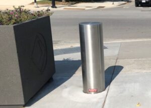 Stainless steel bollard cover over a bollard on a sidewalk.